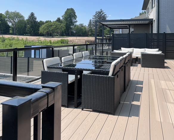 Vinyl deck with patio furniture, surrounded by glass railing and backyard view.